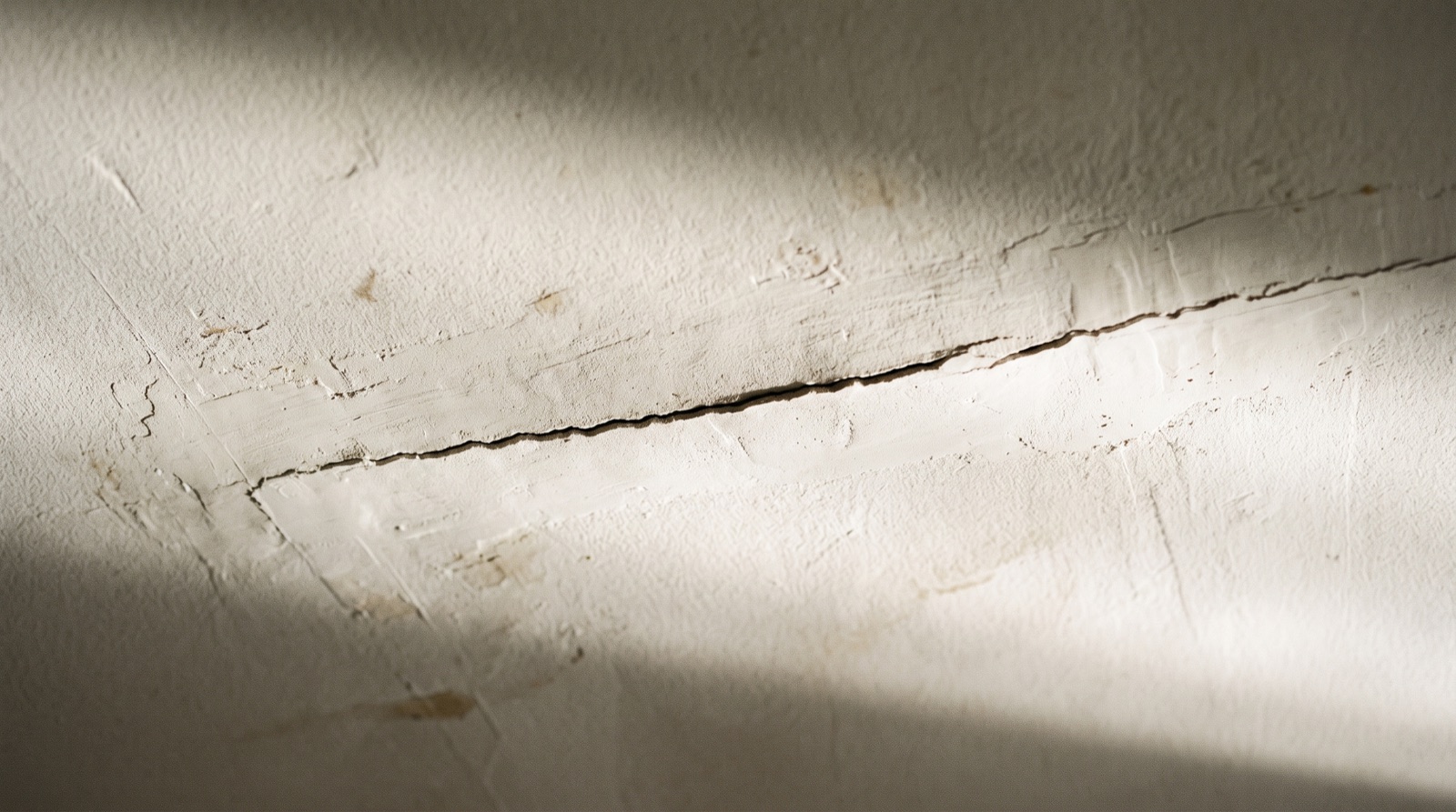 Fissure fine visible au plafond d'une pièce, éclairage rasant révélant le relief